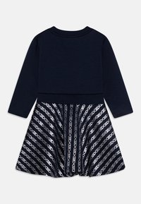 Marineblauwe lange jurk met een effen bovenkant en een uitlopende rok met een diagonaal zilveren kettingpatroon.