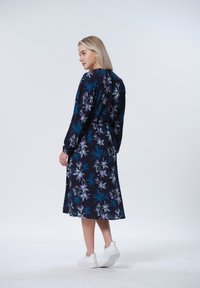Navy sininen kukkakuosisettu mekko, jossa on pitkät hihat, vyö vyötäröllä ja lentävä hame. Yhdistetty valkoisiin tennareihin. Sujuva kangas rakenne.