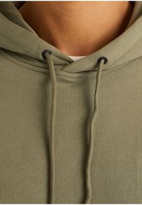 Felpa verde in cotone con cappuccio e lacci, caratterizzata da un tessuto testurizzato e un design rilassato; include dettagli di cucitura visibili e accessori metallici.