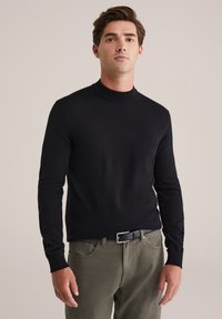 Pulover negru cu mânecă lungă și guler tip tunică, cu o textură moale, asortat cu pantaloni verzi măslinii, detaliu cu cataramă argintie.