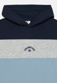 Hættetrøje i marineblå, grå og lyseblå. Har specifik syning og et "Champion" logo broderet i marineblå. Blød tekstur.