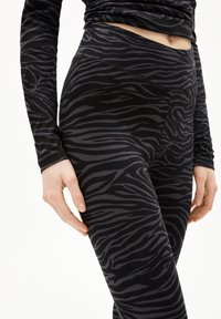 Zwarte legging met een zebra-strepenpatroon in donkergrijs. De stof lijkt zacht met een gladde textuur en heeft een hoge tailleband.