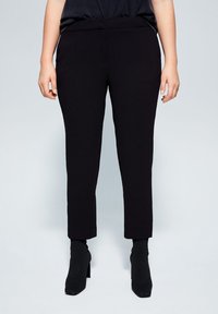 Pantalon noir sur mesure à coupe ajustée, avec une texture lisse et une taille mi-haute, associé à des bottines à talons montant jusqu'à la cheville.