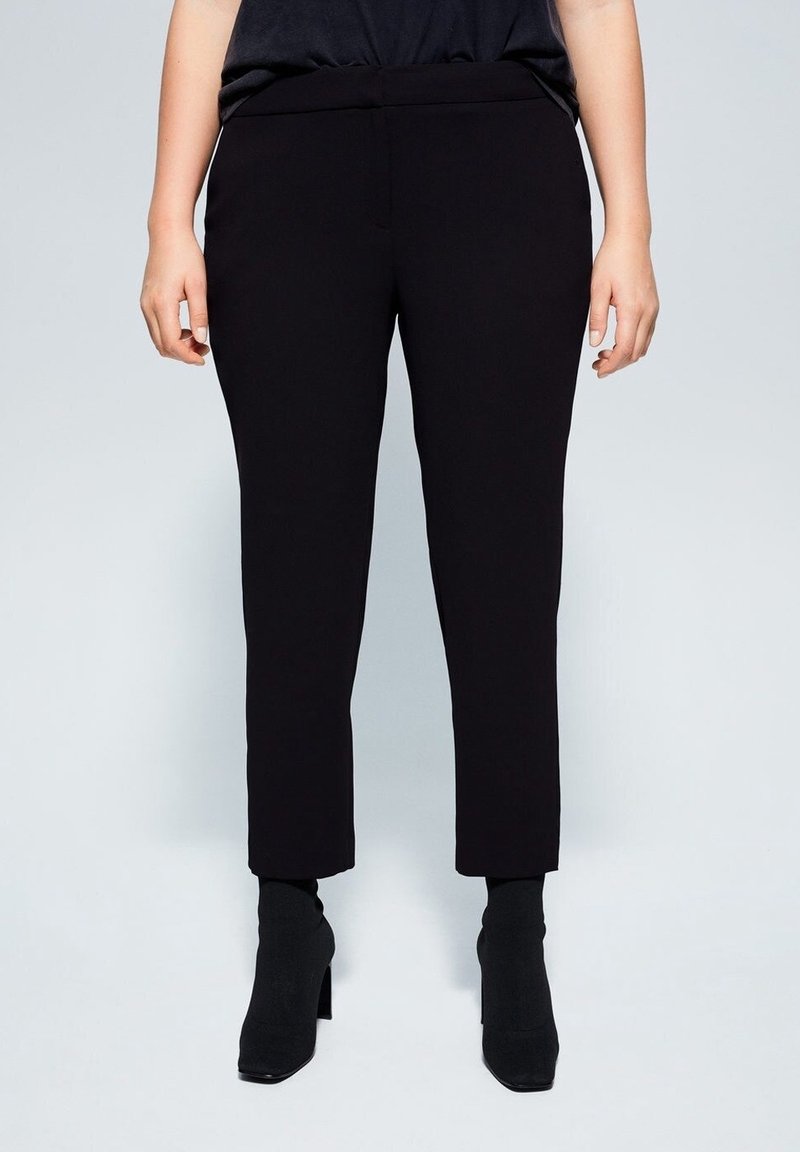 Pantalon noir sur mesure à coupe ajustée, avec une texture lisse et une taille mi-haute, associé à des bottines à talons montant jusqu'à la cheville.