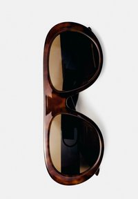 Lunettes de soleil oversize marron écaille avec des verres rectangulaires arrondis sur fond blanc.