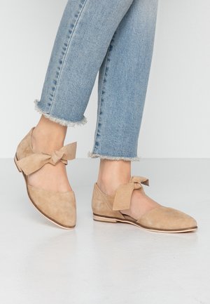 Beżowe zamszowe baleriny z wąskim noskiem, związane ozdobne kokardki po bokach i płaska podeszwa. W połączeniu z jasnoniebieskimi dżinsami z postrzępionym dołem.