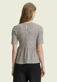 Schwarzes und weißes gepunktetes Peplum-Oberteil mit kurzen Ärmeln, Rückenöffnung und weichem Stofffinish. Kombiniert mit schwarzen Hosen.