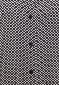 Blus med svartvita prickar som har en knappstängning med fyra svarta knappar framtill. Mjukt tyg med en slät textur.