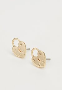 Boucles d'oreilles en or en forme de cœur, conçues comme des cadenas, avec une finition lisse, un détail de trou de serrure et de petits accents en forme de point à la surface.