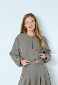 Grau gekürzte Jacke mit Reißverschluss und Puffärmeln, kombiniert mit passenden, hoch taillierten, plissierten Hosen. Glatter Stoff und strukturierte Passform.