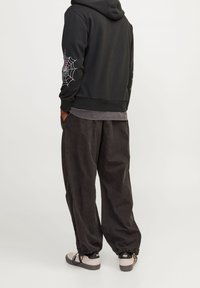 Sudadera negra con capucha y diseño de telaraña en las mangas, combinada con pantalones sueltos de color gris carbón y sandalias grises.