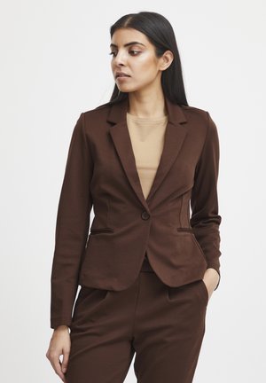 Brun blazer i en figursyet model med enkelt knaplukning, ridsede revers og forlommer; kombineret med en beige top og bukser.