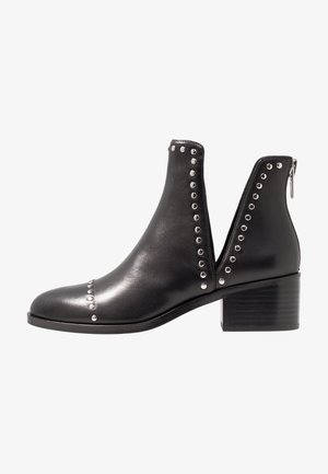 Bottines en cuir noir avec des clous métalliques, des côtés découpés et un talon épais. Elles possèdent une fermeture éclair à l'arrière pour un enfilage facile.