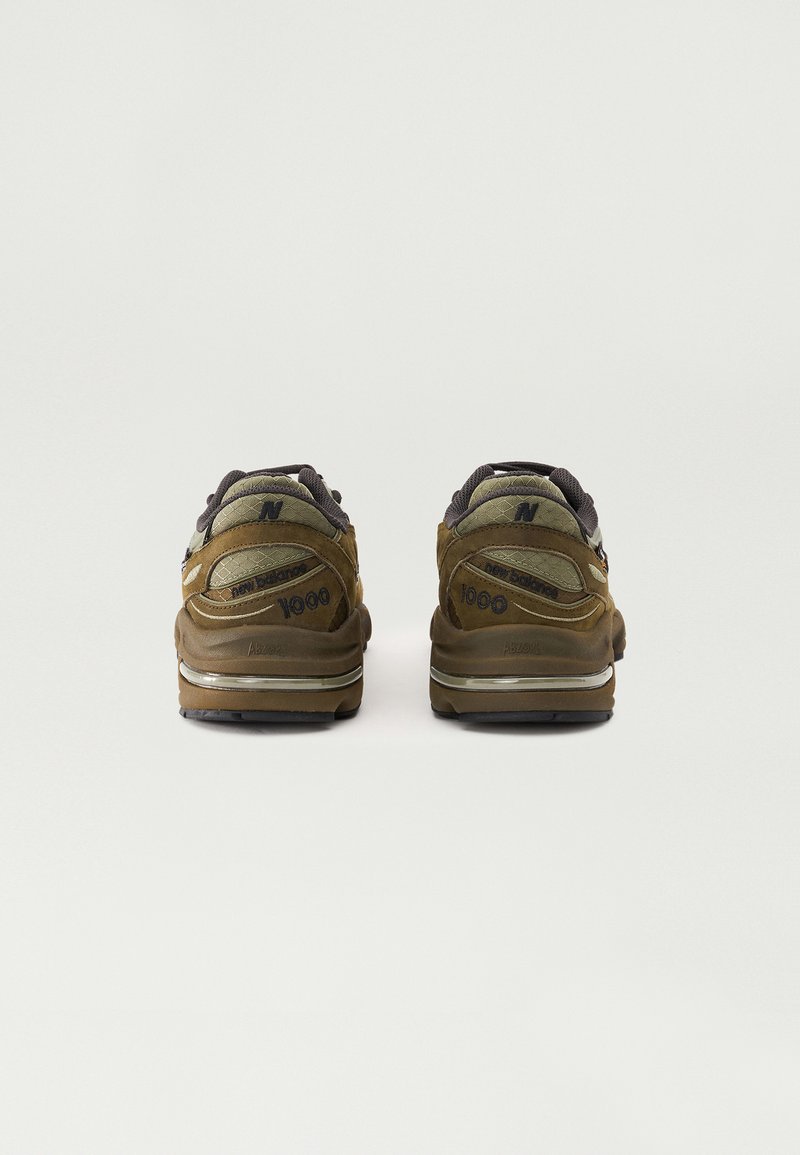 Sneakers New Balance 1000 marroni con una tomaia in suede texture, accenti grigio scuro e una suola intermedia ammortizzata con dettagli riflettenti.