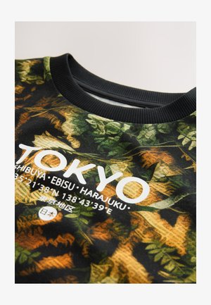 Črna majica s kapuco z zeleno-rjavim listnatim vzorcem. Na sprednji strani ima bel napis "TOKYO" in koordinate. Črni ovratnik z rebrastim vzorcem.