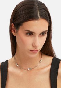 Sølvfarvet choker-halskæde med glatte metalliske perler og skinnende hvide perler, designet med en tynd, fleksibel metaltråd.