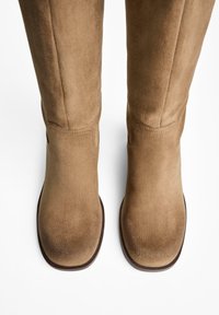 Knee-high brown suede boots with a smooth texture, rounded toe, stitched details, and a solid sole. Designed for comfort and warmth.