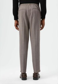 Grijze, gestructureerde broek met een elastische tailleband, achterzakken en taps toelopende pijpen, gecombineerd met bruine nette schoenen.