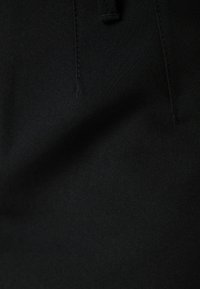 Svart tyg med en slät textur, som har subtila stygn detaljer och en avsmalnande form, lämplig för skräddarsydda kläder.