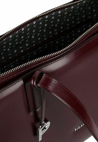 Bordeauxrode leren handtas met een ritssluiting, zwart patroon voering en zilveren sieraccenten. Glad oppervlak met een gestructureerde vorm.