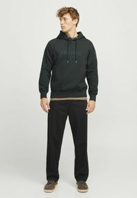 Dark green hoodie with a front pocket, featuring the word "ORIGINALS" in black. Paired with black pants and brown shoes.