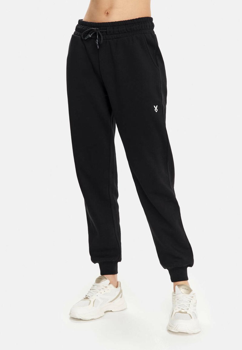 Schwarze Sweatpants aus weichem Material, mit einem elastischen Bund und Bündchen, sowie einem kleinen weißen Logo am linken Oberschenkel.