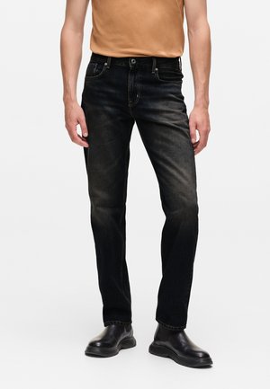 Schwarze Jeans aus Denim mit geradem Schnitt, ausgestattet mit einem klassischen Fünf-Taschen-Design und subtilen Verwaschungen. Kombiniert mit einem beigen Shirt und schwarzen Stiefeln.