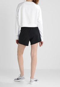 Sudadera blanca corta con mangas largas, combinada con pantalones cortos deportivos negros y zapatillas grises. Textura suave, ajuste cómodo.