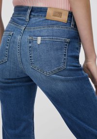 Tumesinised teksapüksid tekstuurse viimistlusega, mille vöökohal on pruun nahast silt ja tagataskutel metallist detailid.