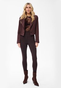 Bruine krijtstreep cropped blazer over een doorzichtige, bloemrijke top, gecombineerd met strakke bruine leggings en bruine suède enkellaarzen.