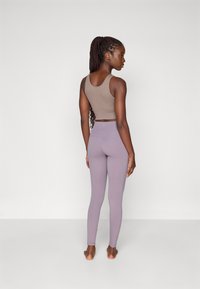 Brown sports bra and light purple leggings, seamless design, fitted shape, soft texture, worn barefoot, long braided hair.