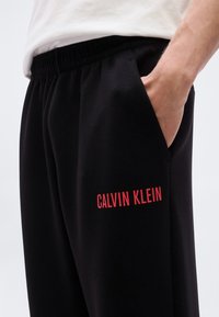 Μαύρα παντελόνια jogging με ελαστική μέση και πλαϊνές τσέπες, με κόκκινο λογότυπο "CALVIN KLEIN" στο αριστερό πόδι. Λείο ύφασμα.