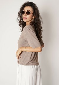 Jasnobrązowa koszulka z krótkim rękawem, luźny krój i miękka tekstura. Zestawiona z białymi spodniami i okrągłymi okularami przeciwsłonecznymi. Akcenty w postaci srebrnej biżuterii.