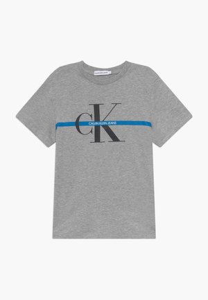 T-shirt gris à manches courtes avec une bande horizontale bleue et de grandes lettres noires "CK" avec le texte "Calvin Klein Jeans" sur la poitrine.