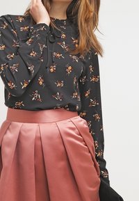 Svart blommig blus med långa ärmar, med en knytning i halsringningen. Satin, plisserad blush rosa kjol. Båda plaggen har en jämn yta.