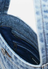 Hellblaues Denim-Taschen mit strukturiertem Design, das über ein dunkelblaues Innenfutter und eine schwarze Reißverschlusstasche verfügt. Robuste Nähte sind sichtbar.