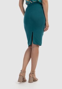 Fustă midi teal, cu dungi, având o deschidere la spate, asortată cu sandale cu toc bloc bej. Textură netedă și design ajustat.