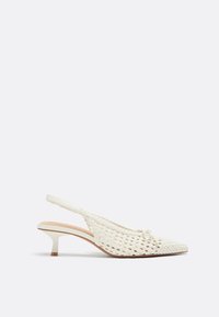 Chaussure blanche à talon bas kitten, tissée, avec bride arrière, bout pointu et petit détail de nœud sur le dessus, vue de côté sur un fond uni.