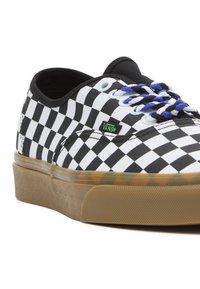 Baskets basses Vans avec motif damier noir et blanc, lacets tressés bleus et blancs, et semelle en caoutchouc marron.