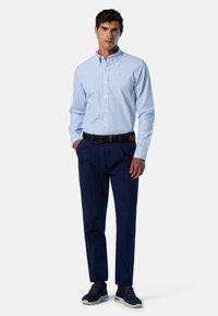 Camisa de rayas azul claro con botones y cuello, pantalones azul marino, cinturón negro y zapatillas deportivas azul marino. El conjunto tiene un ajuste relajado.
