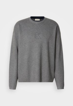 Pilkas megztinis su apvaliu iškirpimu, su įspauduotu "ck" logotipu ant krūtinės ir siaurais rankogaliais. Minkšta tekstūra, laisvas siluetas.