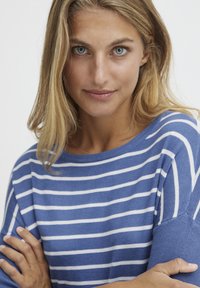 Blau-weiß gestreifter Pullover mit weiter Ausschnitt, kurzen Ärmeln und strukturiertem Strick. Das Model hat die Arme verschränkt und zeigt das Design.