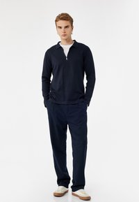Navyblaues, langärmliges Oberteil mit Reißverschluss und Kragen, kombiniert mit passender navyblauer Hose und weißen Turnschuhen. Glatte Textur, lässiges Design.