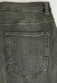 Poche arrière et passants de ceinture d'un jean denim gris foncé avec des détails de couture visibles sur un fond clair.