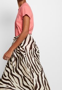 Pink cotton t-shirt with short sleeves paired with a flowing, zebra-striped skirt in cream and brown, tied at the waist.