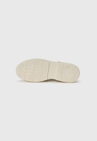 Semelle de chaussure blanche en caoutchouc avec un motif de semelle profond et un logo. Texture lisse avec des motifs floraux et géométriques pour une adhérence et un style. Profil mince.