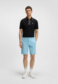 Polo nero con accenti bianchi e logo, abbinato a pantaloni corti blu chiaro. Il modello indossa sneakers bianche e calze a righe.