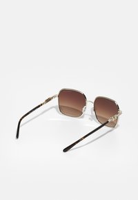 Sunglasses with a brown gradient lens, gold metal frame, and textured tortoiseshell temples featuring a logo accent.