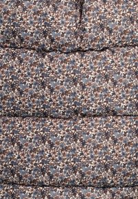 Blommönstrad tyg med en blandning av blå, persika och bruna blommor på en ljus beige bakgrund med kviltad textur.