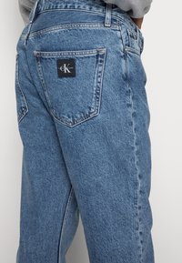 Jeans in denim blu chiaro con vestibilità comoda, dotati di tasche posteriori e una cucitura del logo Calvin Klein nero sopra la tasca destra.